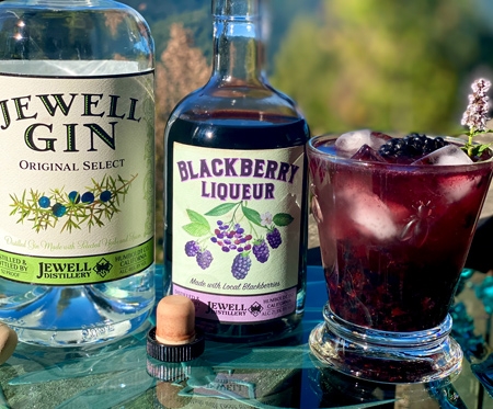 Blackberry liqueur bottle, jewell gin bottle and a rocks glass with a dark red cocktail and blackberries