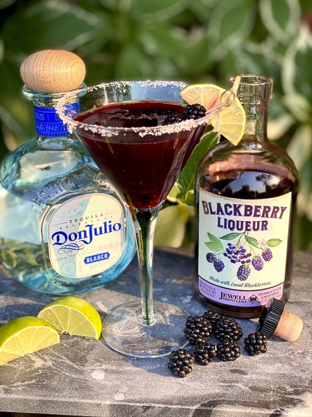 bottles of Don Julio and blackberry Liqueur and a martini glass with a blueberry cocktail in it